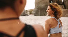 Cheerful women in fitness wear sitting on the beach